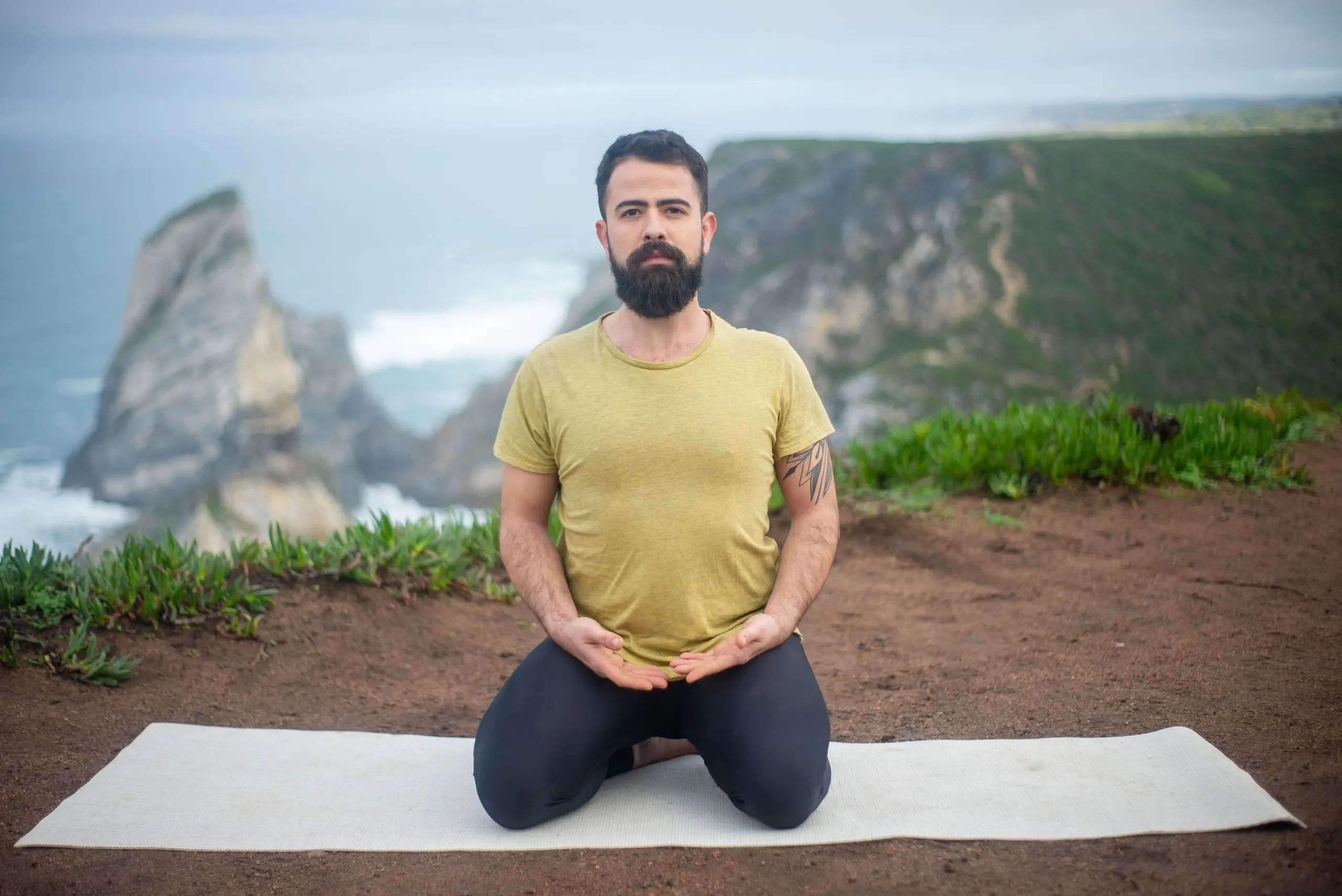 Un homme assis sur un tapis de yoga, face à l'océan
