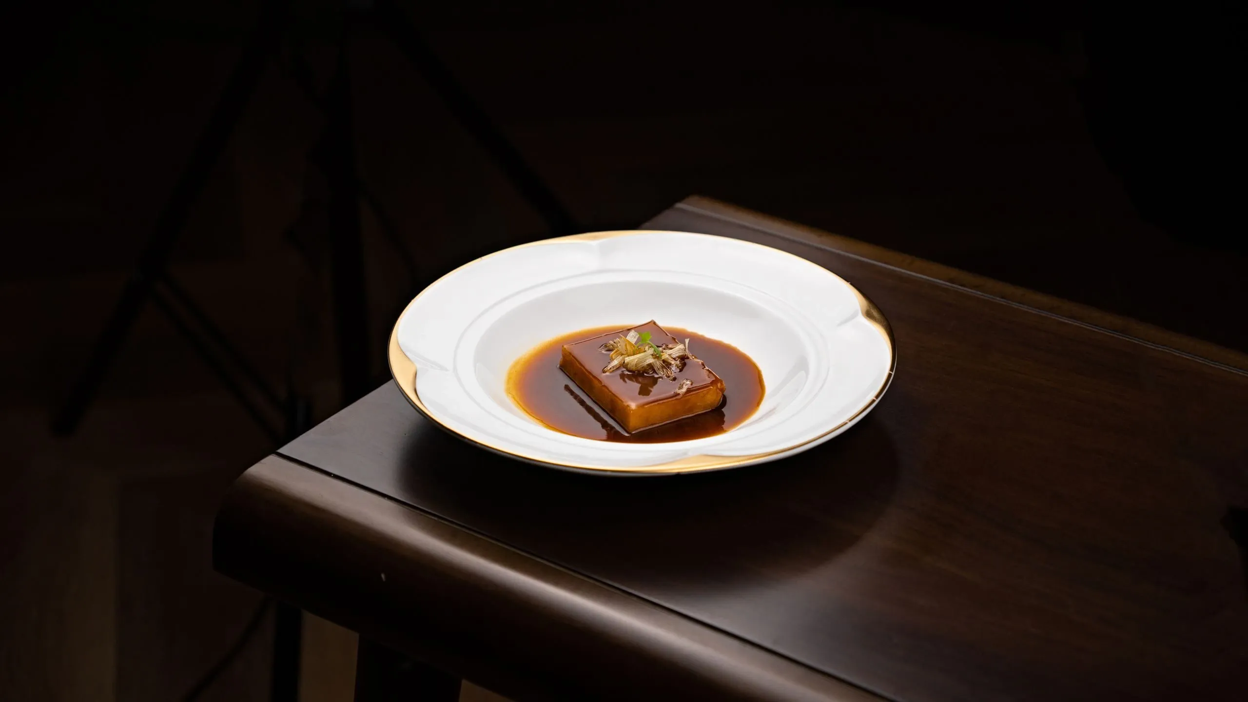 Une assiette gastronomique dressée sur une table en bois, dans la pénombre